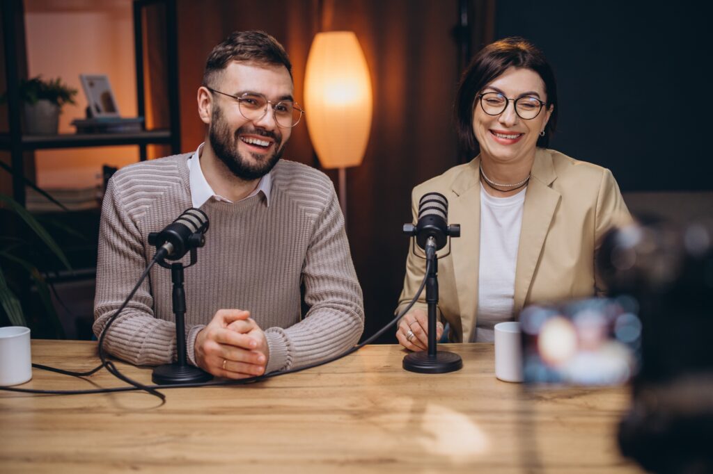 Two happy podcasters, a man and a woman, are recording a new podcast episode in professional studio